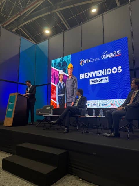 Speaker and seated participants on stage beneath the Colombiaplast welcome screen